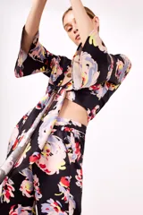 Camisa estampada con flores de colores sobre fondo negro, de corte cruzado, mangas 3/4 acampanadas y escote en V.