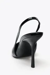 Zapato destalonado acharolado color negro, con tacón fino y punta. Tiene una tira trasera con elástico.