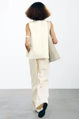Chaleco color crema de punto con cuello redondo y sisa. Tiene botones metálicos dorados en los laterales.