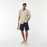 Camisa de manga corta color beige con estampado de palmeras y motivos playeros en negro.