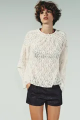 Top de encaje color blanco, con cuello redondo, mangas largas acampanadas y detalle de tachas metálicas en cuello y hombros. Cierre en la espalda con abertura y botón.