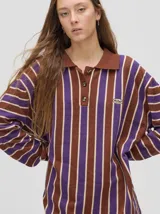 Chomba de corte oversize con cuello camisero, a rayas verticales en color marrón, lila y blanco. Tiene un logo bordado en el pecho y puños en color marrón.