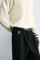 Pantalón gris de corte ancho con cintura elástica, pliegues frontales, bolsillos laterales y traseros de vivo. Incluye detalle de hebilla metálica en la trabilla y cierre frontal con cremallera y botón.