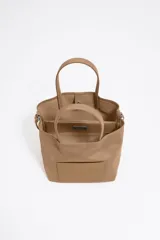 Bolso tote pequeño color marrón claro, de la marca Bimba y Lola, modelo Chihuahua. Tiene doble asa corta y correa larga extraíble. Presenta un bolsillo externo con parche con el logo de la marca.