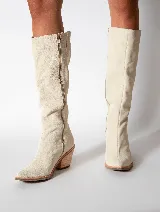 Bota alta color beige de cuero gamuzado, con punta fina y cierre lateral. Tiene un taco de madera con forma geométrica.