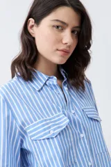 Camisa celeste con rayas verticales blancas, de manga larga y corte clásico, con cuello camisero y dos bolsillos con solapa en el pecho.