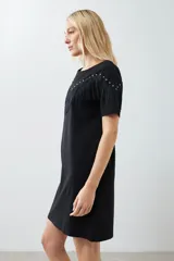 Vestido corto negro con flecos en el pecho y tachas plateadas en los hombros.