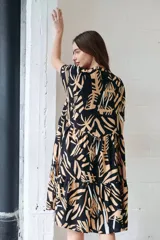 Vestido camisero midi con volados, estampado con hojas en tonos camel, blanco y negro. Tiene cuello redondo, mangas cortas y cierre frontal con botones.