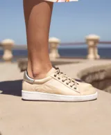 Zapatillas acordonadas de cuero color marrón con detalles dorados en el talón y suela blanca.