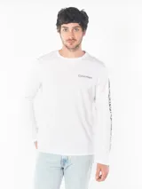 Remera blanca de algodón con cuello redondo y manga larga. Logo de Calvin Klein estampado en el pecho y diseño con letras en la manga.