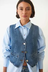 Chaleco denim con botones plateados en la parte delantera y bolsillos simulados.