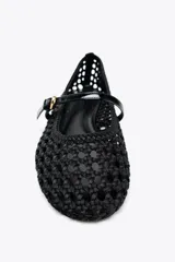 Zapato plano tipo bailarina color negro, con capellada trenzada y tira sobre el empeine con hebilla dorada.