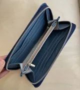 Billetera de cuero color verde pistacho con cierre perimetral y logo metálico de la marca en el frente.