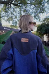 Campera de jean con paneles en azul y negro, cierre frontal con cremallera, mangas largas abullonadas con puños elásticos y un bolsillo asimétrico en el frente.
