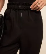 Pantalón negro de sastrería, modelo zanahoria, con tiro alto, cintura elástica con botones y cierre por cremallera. Tiene bolsillos delanteros.