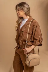 Bandolera de cuero sintético color beige, con diseño compacto y elegante. Cuenta con un bolsillo frontal con cierre y un compartimento principal con cierre. La correa es regulable.