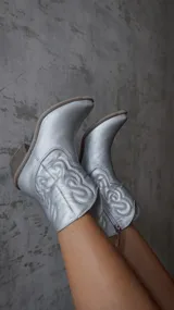 Bota corta plateada de estilo texano con bordados en el caño, taco de madera y cierre lateral.