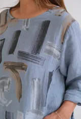 Blusa celeste con estampado abstracto en tonos grises y marrones, de corte holgado y mangas 3/4 con botón.