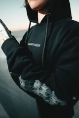 Canguro negro con capucha, bolsillo delantero y estampado de llamas en las mangas.