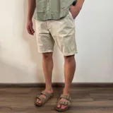 Bermuda color beige claro, estilo chino, confeccionada en gabardina. Presenta un corte recto y dobladillo en el ruedo.