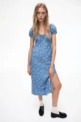 Vestido largo de lino y viscosa color celeste con estampado de flores blancas. Tiene mangas cortas abullonadas, escote corazón con tiras finas, copas preformadas con frunces, elástico en escote, hombros, mangas y cintura, cierre lateral oculto y tajo pronunciado en un lado.