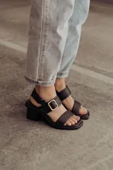 Sandalia de cuero color negro con taco bloque medio y punta cuadrada. Presenta dos tiras anchas sobre el empeine, una de ellas con hebilla metálica dorada, y una tira de sujeción en el talón. Posee base acolchonada para mayor comodidad.