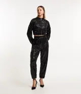 Campera bomber corta negra cubierta de lentejuelas metalizadas, con cuello alto, mangas largas, puños y bajo elásticos, y cierre frontal con cremallera.
