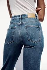 Pantalón de jean gris oscuro, de corte mom fit, tiro alto y largo tobillero. Cuenta con cinco bolsillos, cierre frontal con cremallera y botón.