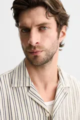 Camisa de hombre relaxed fit confeccionada en tejido de algodón a rayas verticales blancas y negras. Tiene cuello bowling, manga corta, bajo con aberturas laterales y cierre frontal de botonadura.