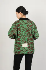 Campera de jean con cuello clásico, cierre frontal con botones metálicos, dos bolsillos de parche en el pecho y estampado floral en tonos verdes y marrones.