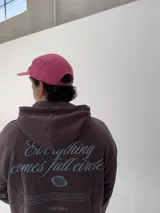 Gorro tipo gorra color fucsia con visera, y estampado frontal en azul con la palabra "attitude" y otros textos.