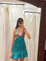 Vestido corto de lentejuelas color verde oliva, con escote en V, breteles finos cruzados en la espalda, cut-outs laterales y volado en el ruedo.