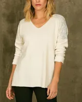 Sweater blanco de lanilla con cuello en V y mangas largas. Presenta apliques de strass en los hombros.