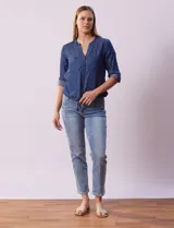 Blusa de tencel azul con cuello a la base y escote en V, abertura central con botones, bolsillos delanteros, mangas 3/4 regulables con presilla y botón, y terminación de ruedo con nudo.