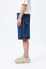 Bermuda carpenter de denim negro, corte relajado y largo a la rodilla, con costuras visibles y múltiples bolsillos funcionales.