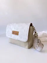 Bandolera color crudo con solapa de gamuza y cuerpo de cuero sintético texturizado. Tiene correa corta de cuero con tientos y forro de tela con bolsillo interno.
