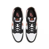 Zapatilla de corte bajo Nike Dunk Low Retro, con base blanca y superposiciones de cuero negro. Presenta el logo Swoosh y detalles en color naranja quemado (burnt orange) en el lateral, talón y suela exterior.