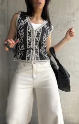 Chaleco negro con bordado floral blanco, escote en V, cierre frontal con botones y ribete de encaje.