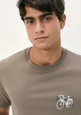 Camiseta blanca de algodón con cuello redondo y mangas cortas. Estampa rectangular con borde negro que contiene la frase "NATURAL ATMOSPHERE" en letras mayúsculas y una imagen de montañas y mar.
