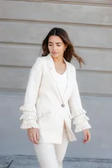 Blazer color beige confeccionado en lino, con cuello solapa, cierre frontal con un botón y mangas largas con volantes en capas.