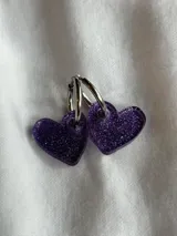 Par de aros colgantes con forma de corazón color violeta con glitter, unidos a un aro de acero plateado.