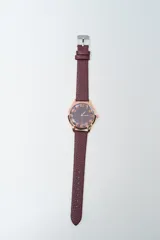 Reloj analógico con caja redonda de metal color oro rosado y correa de cuero texturizado color bordó. La esfera es oscura con números arábigos en tono oro rosado.