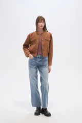 Campera estilo bomber corta de gamuza color marrón, con cuello redondo, cierre frontal de botones y dos bolsillos de parche con solapa en el pecho. Presenta puños y cintura elásticos.