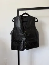 Chaleco negro de cuero con diseño patchwork, cuello en V y cierre frontal con botones dorados. Posee bolsillos delanteros ribeteados.