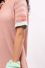 Vestido corto tipo remerón color rosa, de tejido de punto con cuello redondo y mangas cortas. Presenta ribetes en color amarillo en el cuello, celeste en las mangas y naranja en el ruedo.