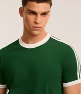 Remera de algodón de corte regular, color blanco hueso, con cuello redondo y ribete negro. Presenta un diseño de doble raya negra en las mangas y ribetes negros en el cuello y los puños de las mangas.