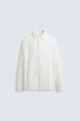Camisa de algodón color blanco hueso, de corte relajado (relaxed fit), con cuello solapa y manga larga terminada en puño con botón. Cierre frontal con botonadura.