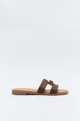 Sandalias planas color marrón con dos tiras anchas en el empeine unidas por un aplique metálico dorado.