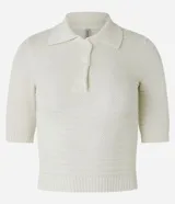 Blusa de punto color crema, con cuello polo, mangas cortas y puños con botones.