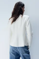 Saco blanco de punto bouclé con cuello redondo, botones forrados hasta la cintura y corte acampanado en la parte inferior.